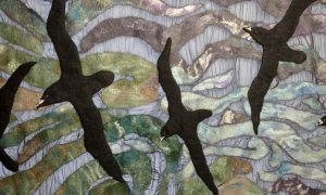 Punakaiki Petrels artwork. This picture depicts 3 Black Petrels in flight. The background shows waves of green, blue and grey with shimmery elements. Made from felting.